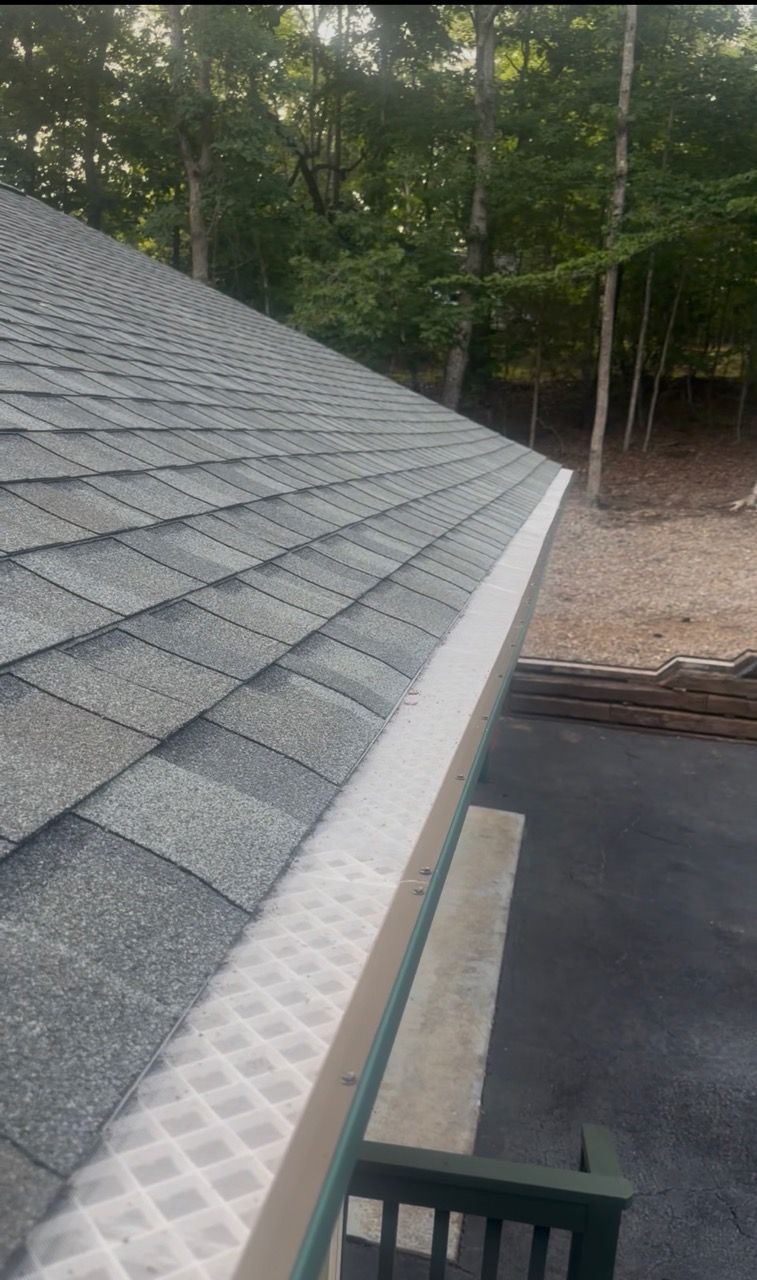New white micromesh gutter guard running along a shingle roof edge backed by Upstate woods